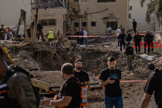 一群身着深色衣物的工作人员站在以色列境内一处地面弹坑旁，此前伊朗导弹在此发动袭击。周六，以色列埃什托尔镇袭击现场的应急救援人员。